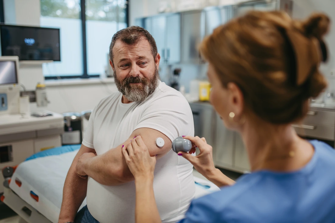 Doctor applying a continuous glucose monitor sensor on patients arm Obese, overweight man is at risk of developing type 2 diabetes Concept of health risks of overwight and obesity