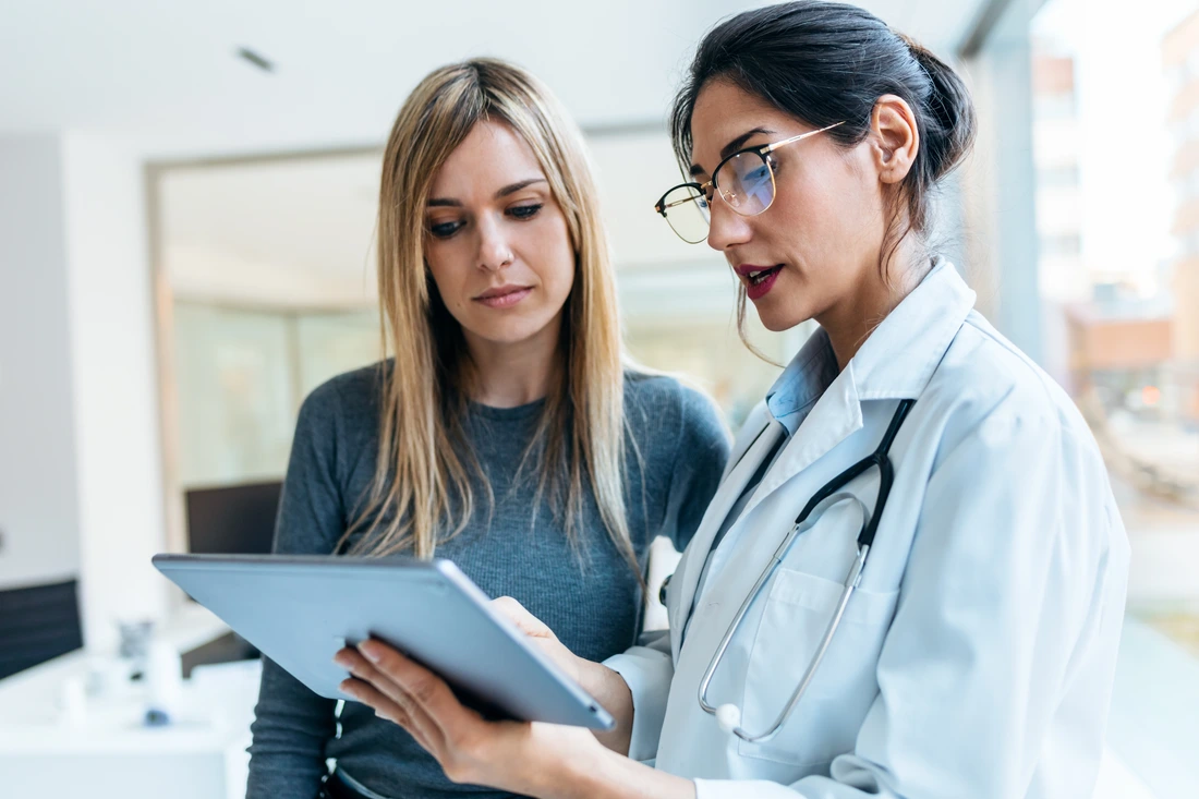 Shot of beautiful female doctor talking while explaining medical treatment with digital tablet to patient in the consultation