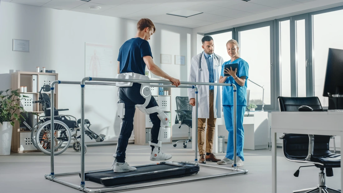 Modern Hospital Physical Therapy Patient with Injury Walks on Treadmill Wearing Advanced Robotic Exoskeleton Physiotherapy Rehabilitation Scientists, Engineers, Doctors use Tablet Computer to Help jp