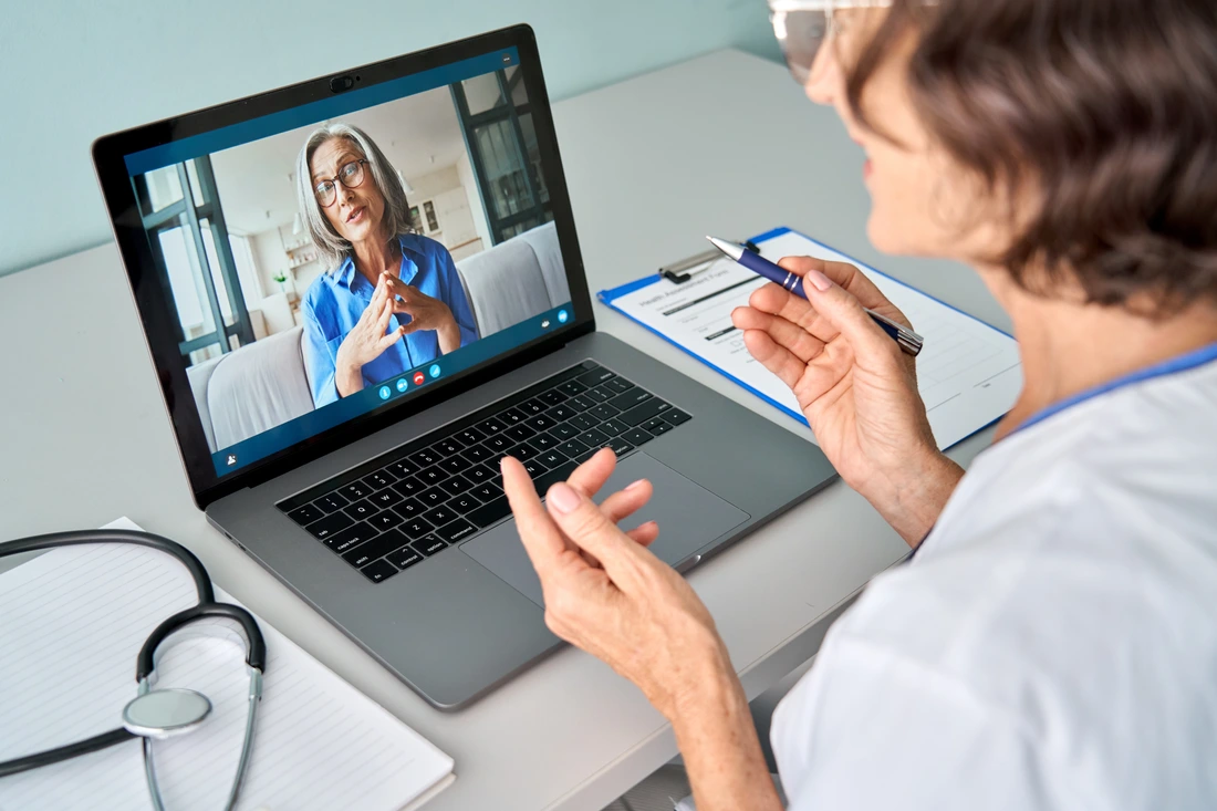 Female doctor therapist consulting older senior patient via virtual video call visit using laptop computer Digital online healthcare, distance telemedicine Telehealth videocall Over shoulder view j