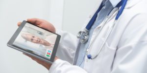 doctor in lab coat talking to elderly woman on ipad