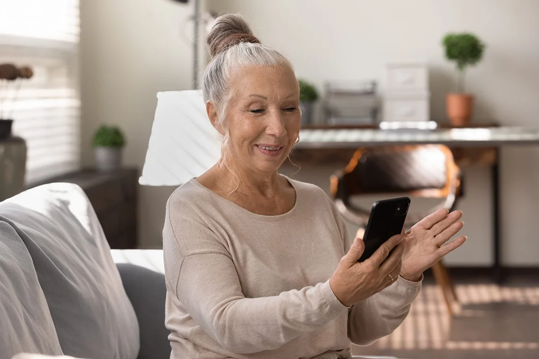 Happy elderly grey haired lady using smartphone at home, making video call, talking to family, relatives online Senior patient consulting doctor at virtual meeting on mobile phone, smiling at screen