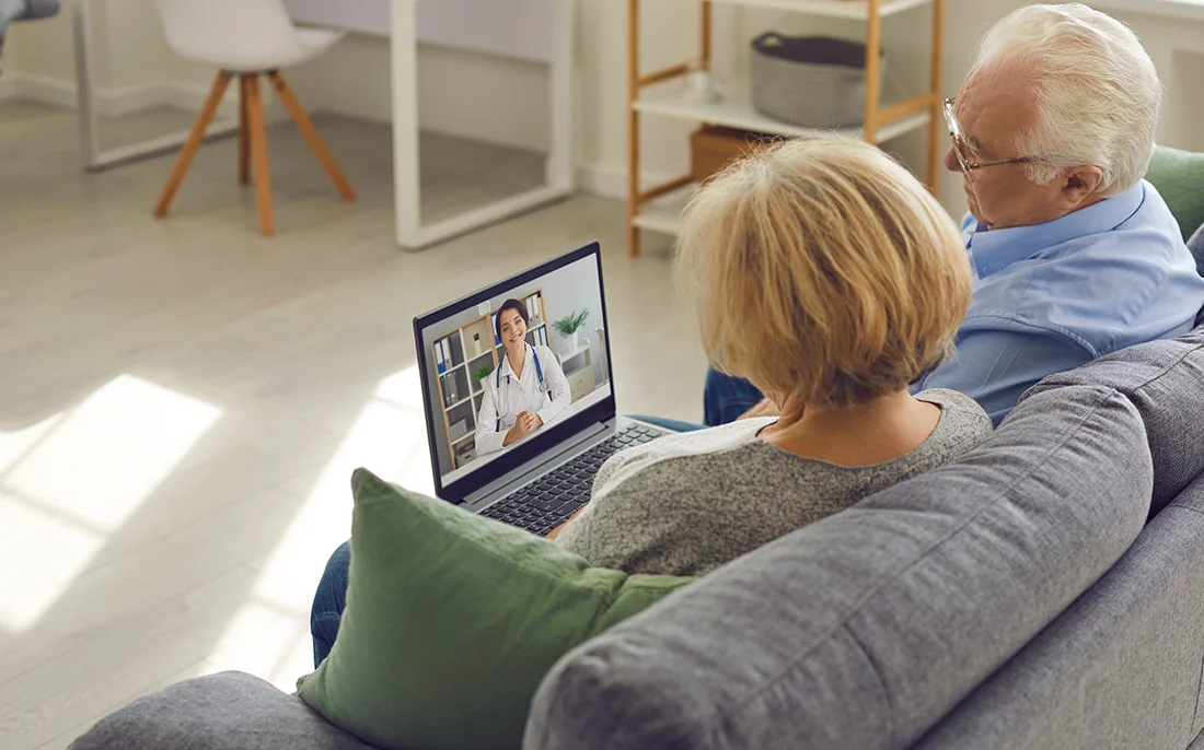 Using eHealth and telemedicine services at home Couple of senior patients sitting on sofa with laptop, having video call with online doctor and getting professional health consultation